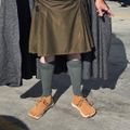 Person wearing olive green kilt, knee-high socks, and brown lace-up shoes standing on concrete pavement