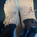 Pair of tan suede moccasin-style shoes with white laces and decorative stitching, photographed from above against a dark background.