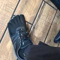 Person wearing black hiking boots with white laces and black pants standing on wooden flooring with dark grout lines.