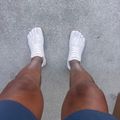 A person wearing white sneakers and blue shorts standing on a gray concrete surface, photographed from above.
