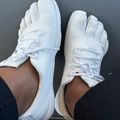 Pair of white mesh sneakers with white laces worn on feet, viewed from above against a dark gray surface.