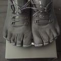 Pair of gray five-finger running shoes with laces displayed on a white box, photographed from above on a dark surface.