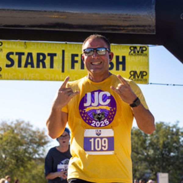 A man wearing a yellow shirt and race bib number 109 celebrates at a race finish line marked by a yellow START/FINISH ba