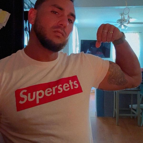 A person wearing a white t-shirt with red text flexing their arm in an indoor setting