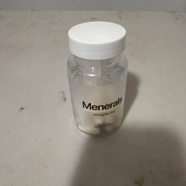 Clear glass supplement bottle with white cap labeled "Menerals" containing white pills or tablets