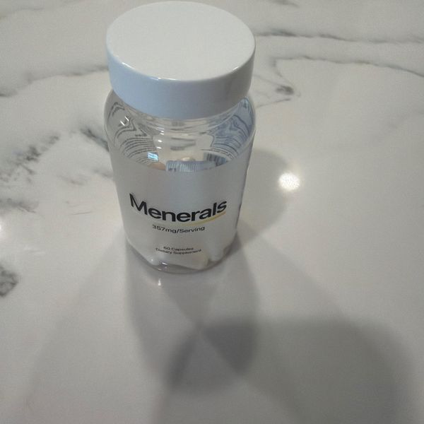 A clear glass bottle with white cap labeled "Menerals" containing 60 capsules, sitting on a white marble surface