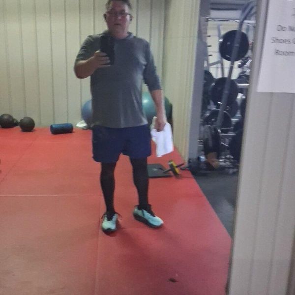 Man in workout clothes standing on red exercise mat in gym holding paper