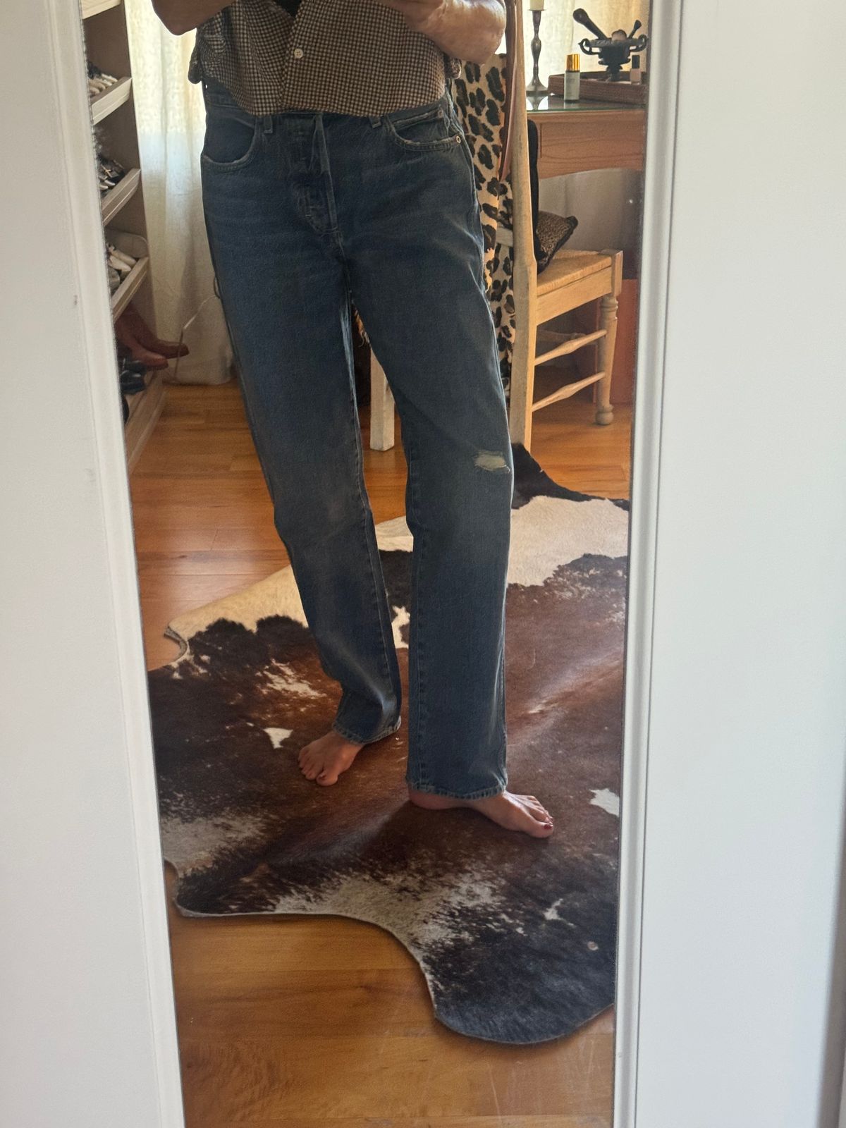 Person wearing jeans and patterned top standing on a cowhide rug in front of a mirror