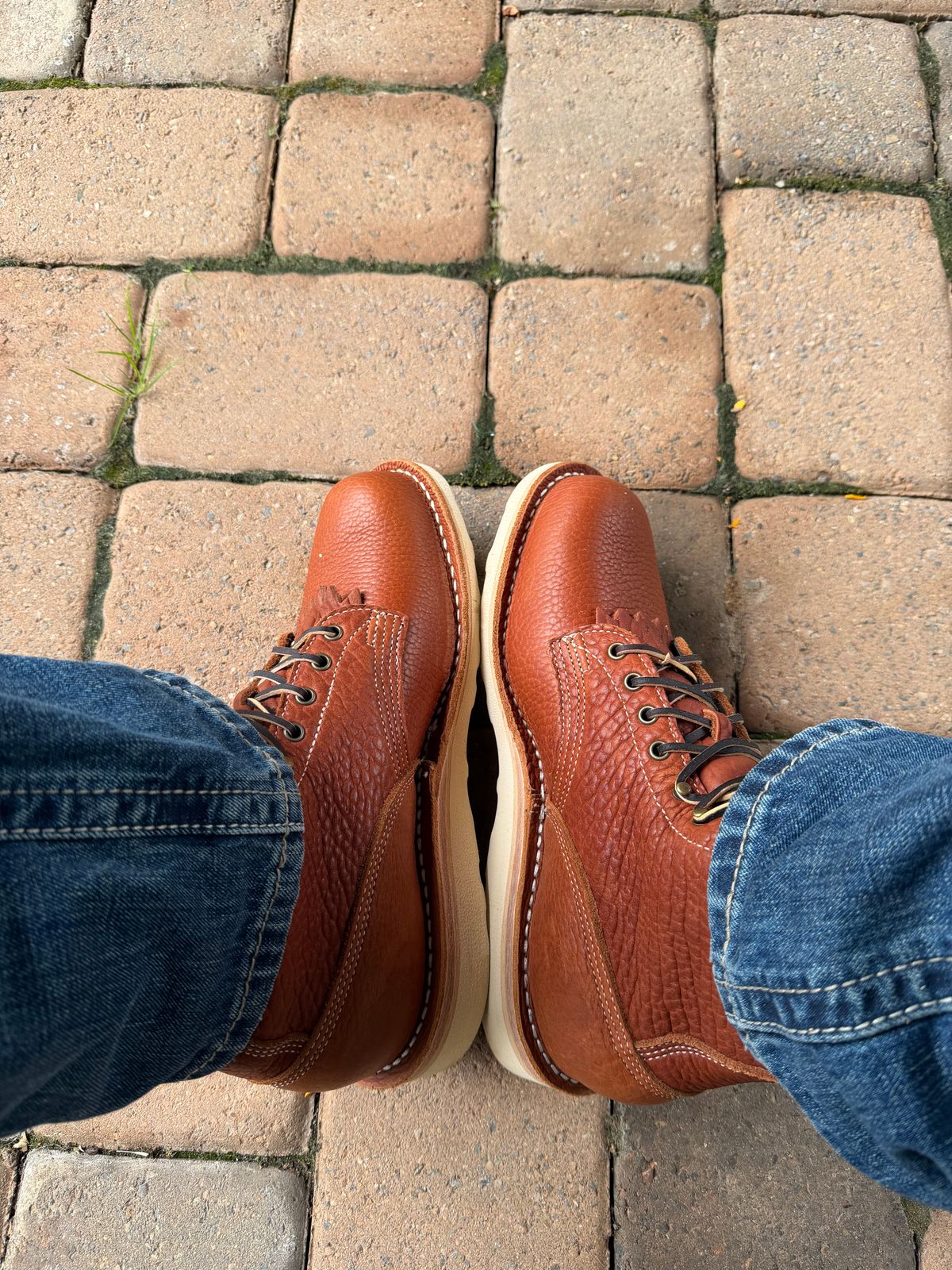 Person wearing brown leather shoes and blue jeans standing on cobblestone pavement