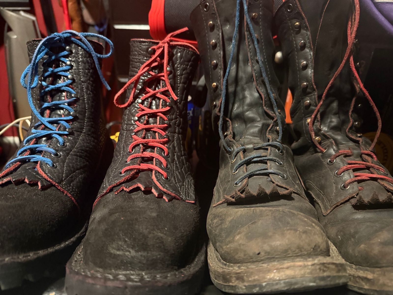 A collection of worn black leather boots with colorful laces including blue and red, arranged together on a surface