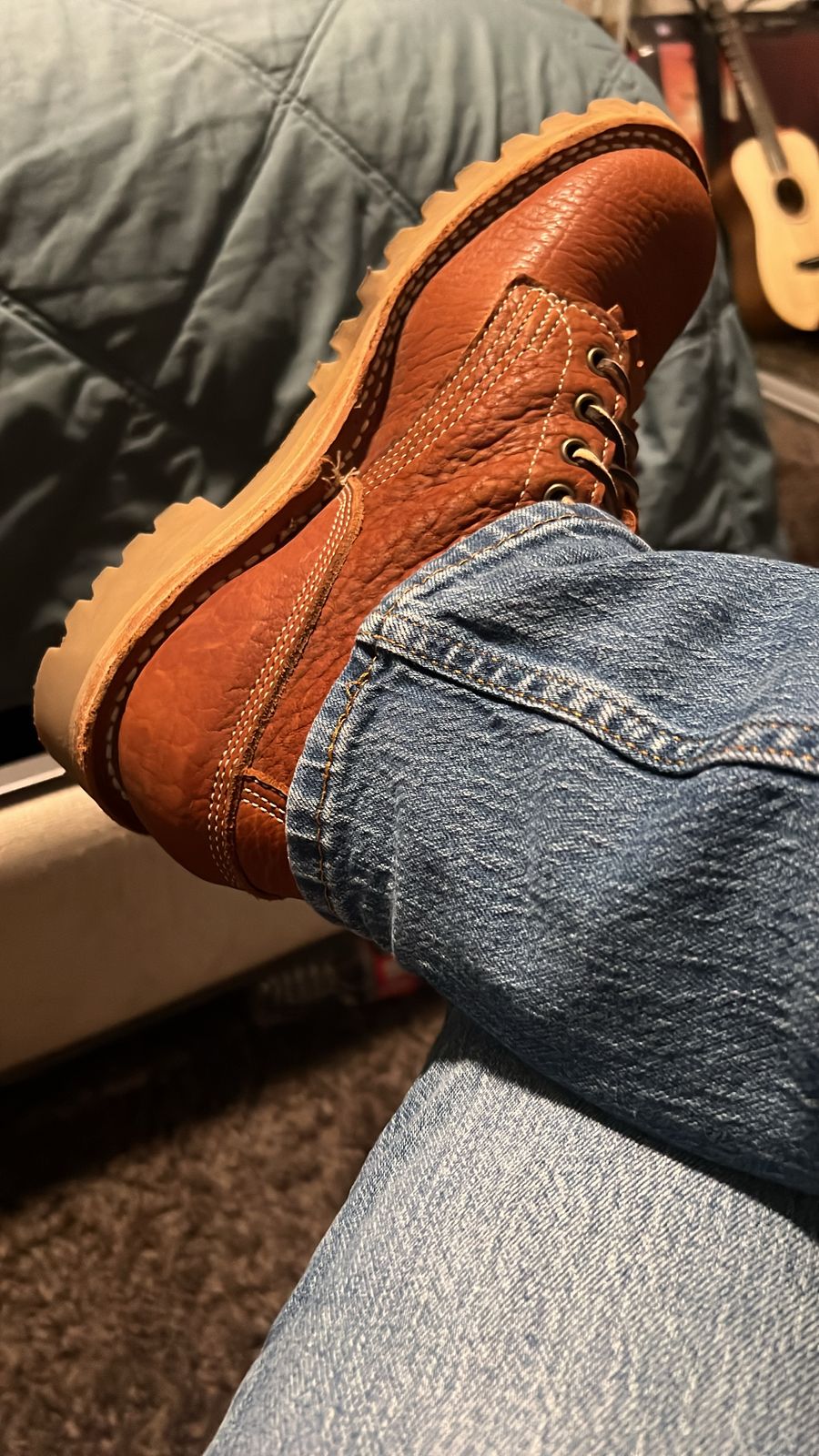 Person wearing brown leather boots with laces and blue jeans, sitting with feet up in a casual indoor setting