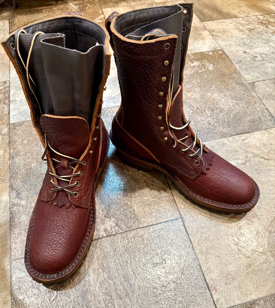 A pair of brown leather lace-up boots with black interior lining sitting on a tiled stone floor