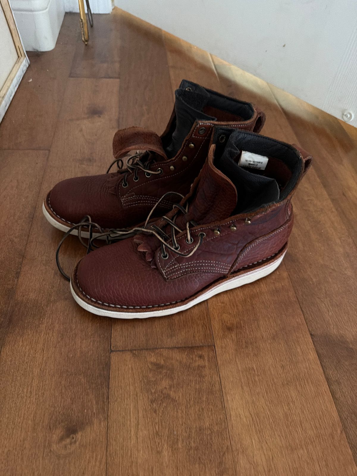 A pair of brown leather work boots with laces sitting on a wooden floor