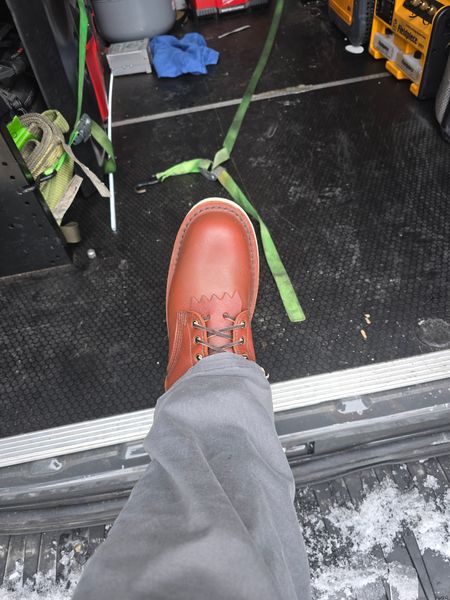 Person wearing brown leather boot standing on metal platform above work area with tools and equipment