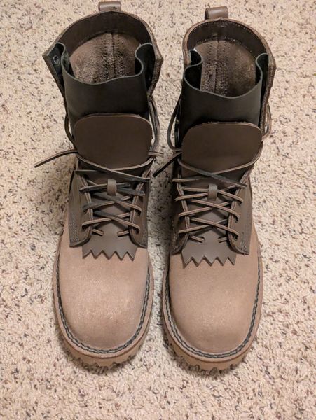 A pair of brown leather hiking boots with laces and ankle support, placed on a textured beige carpet