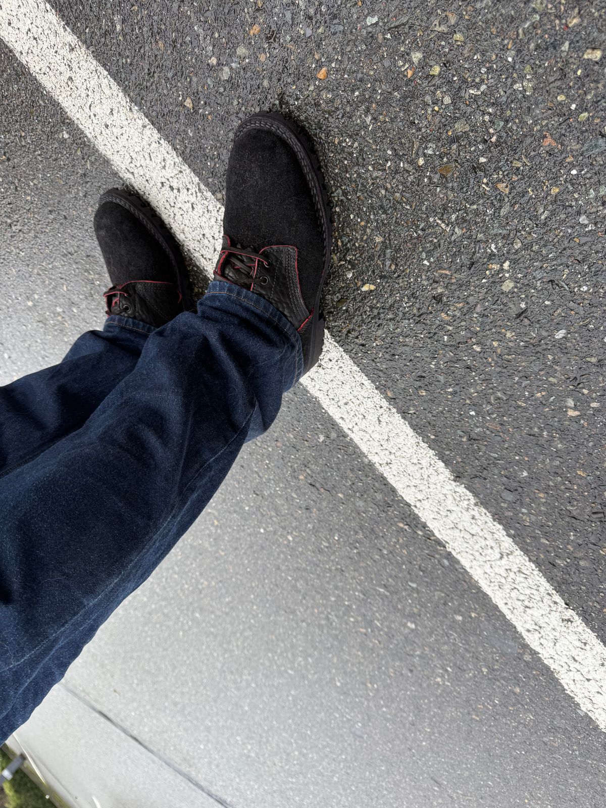 Person wearing black boots and blue jeans standing on asphalt pavement with white painted line
