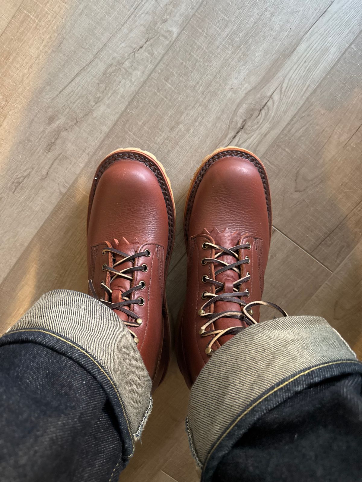 Person wearing brown leather lace-up boots and cuffed jeans standing on wooden flooring