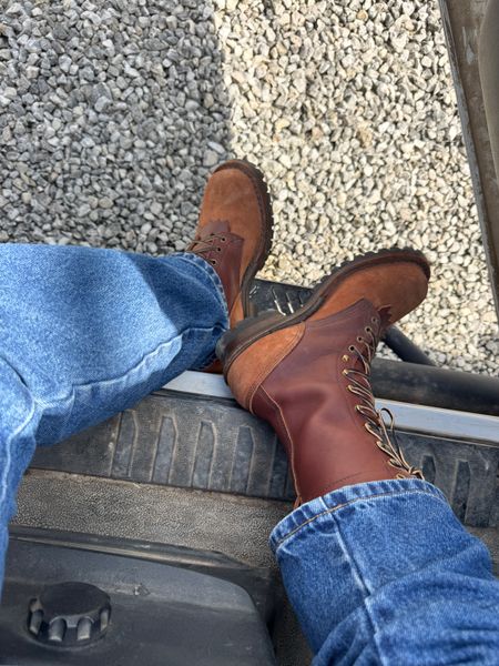 Person wearing brown leather boots and blue jeans sitting on vehicle running board with gravel ground visible below