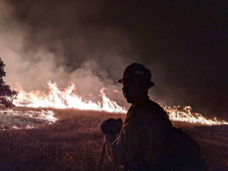Firefighter silhouetted against large wildfire flames and smoke at night