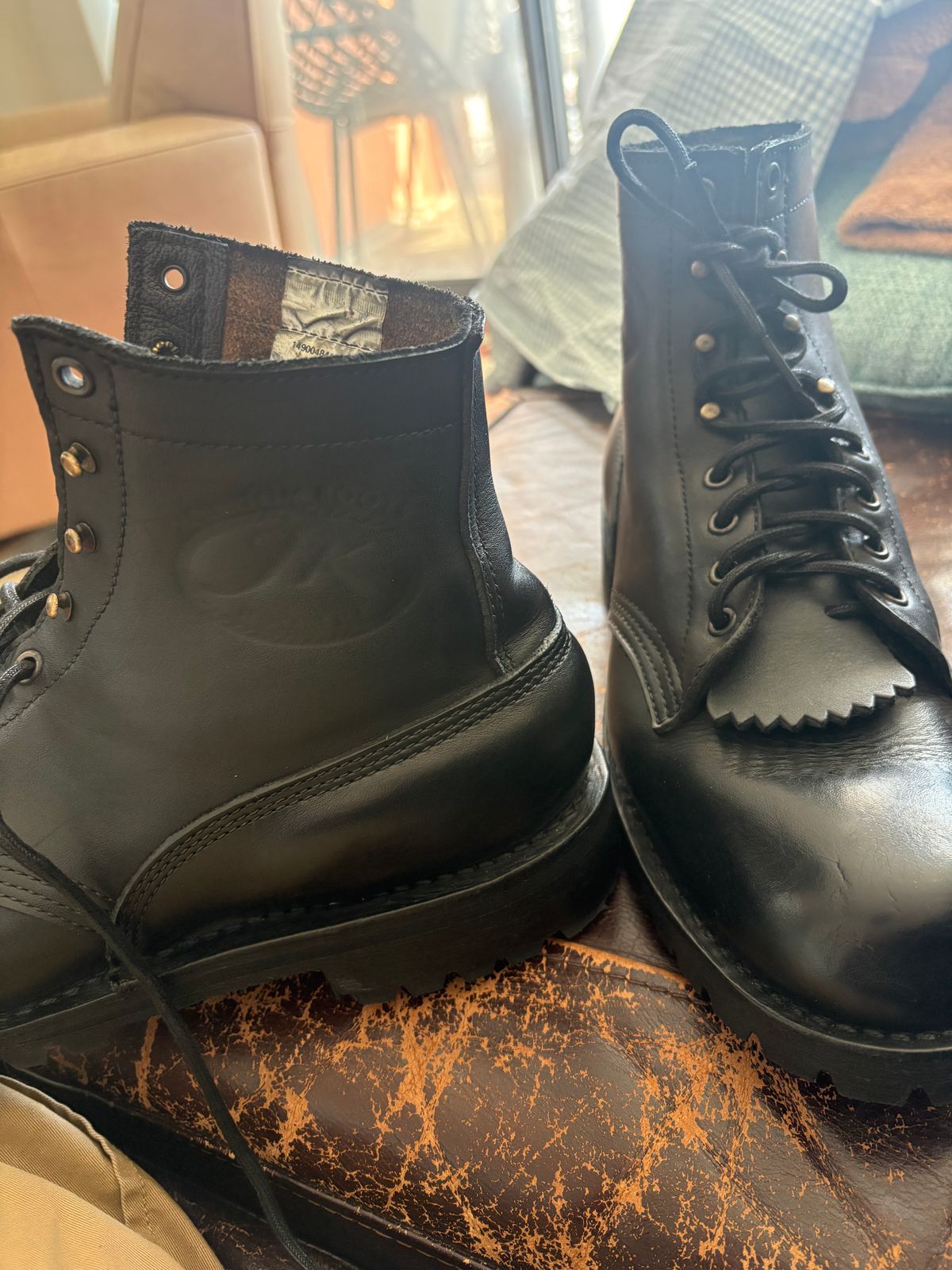 A pair of black leather combat boots with laces sitting on a wooden surface near a fireplace