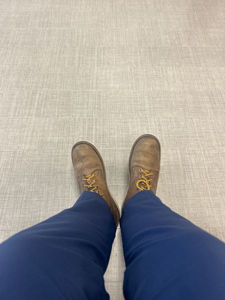 Person wearing blue pants and brown lace-up boots standing on a light-colored textured floor