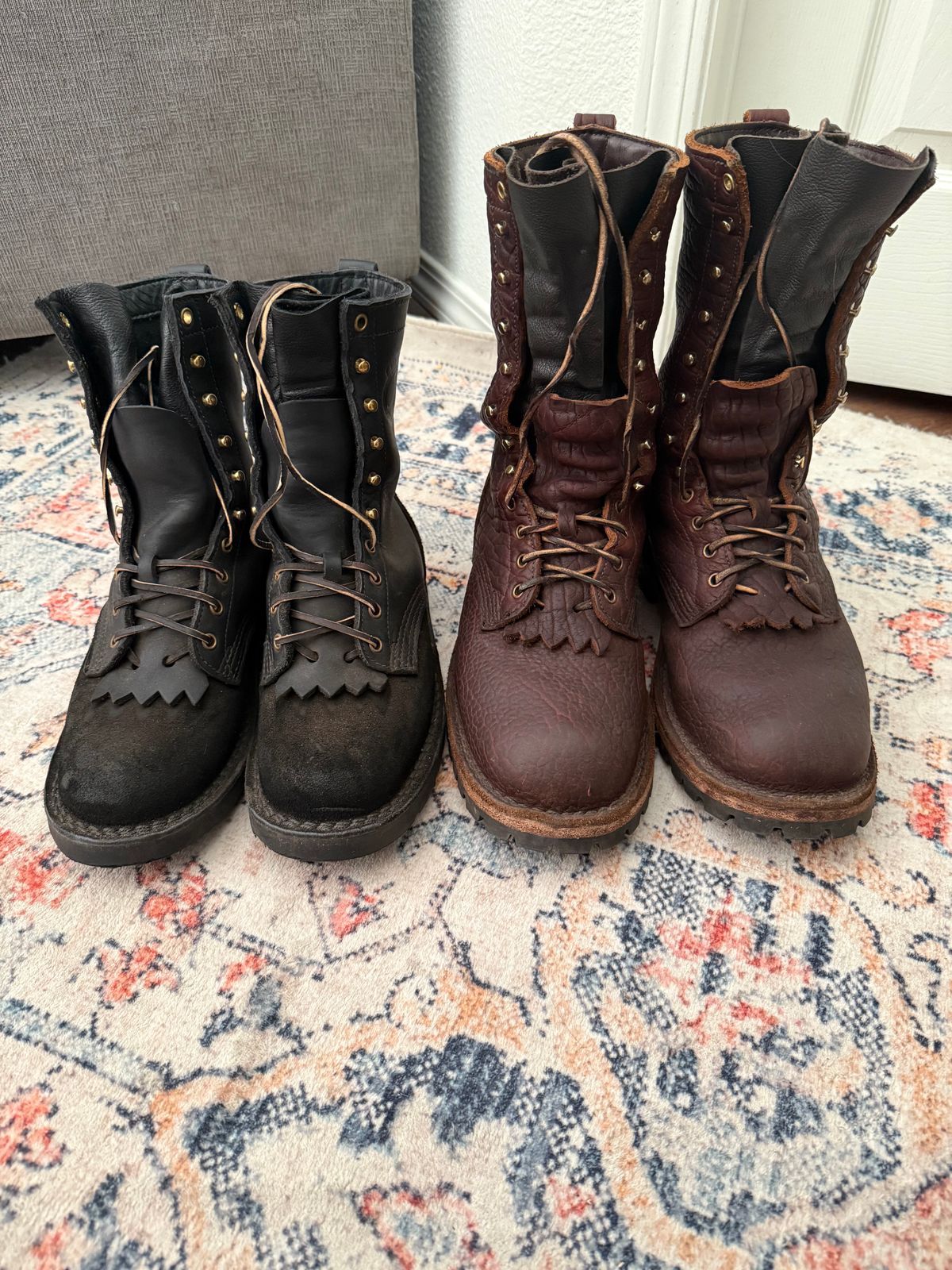 Two pairs of leather boots on a patterned rug - one pair in black and one pair in brown, both with laces and decorative fringe details