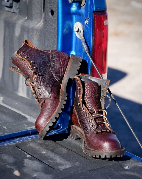 A pair of brown leather work boots with laces sitting on the tailgate of a blue pickup truck
