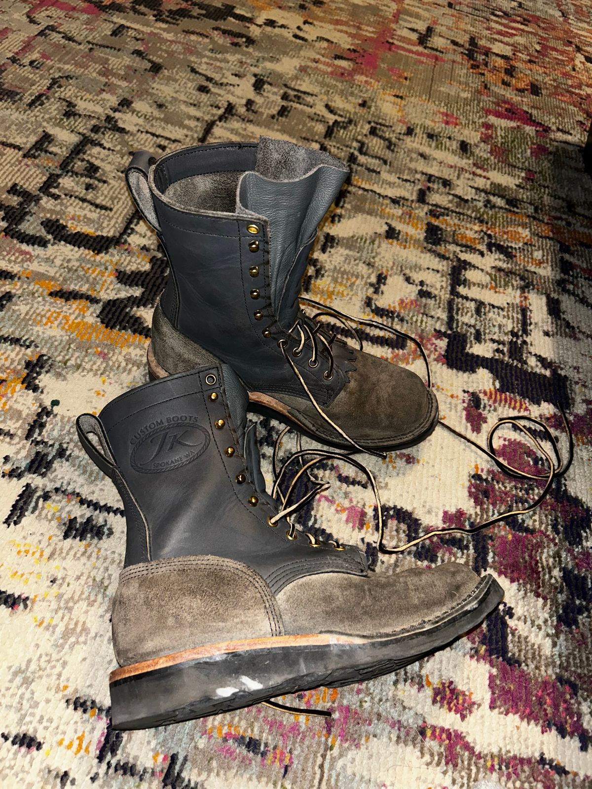 A pair of worn work boots with laces sitting on a colorful patterned rug