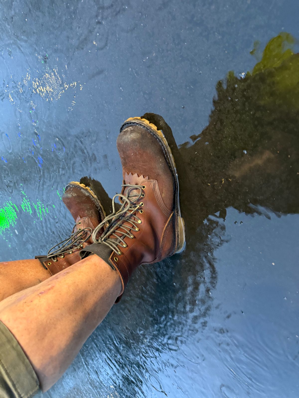 Person wearing brown leather hiking boots with feet dangling in clear blue water