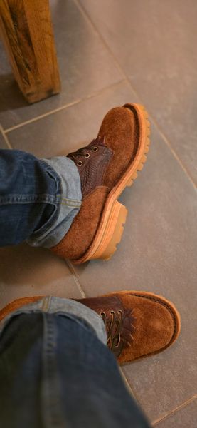 Person wearing brown suede boots with laces and jeans, standing on tiled floor