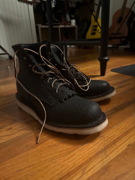 Black high-top sneakers with white laces sitting on wooden floor in a room with musical instruments in the background