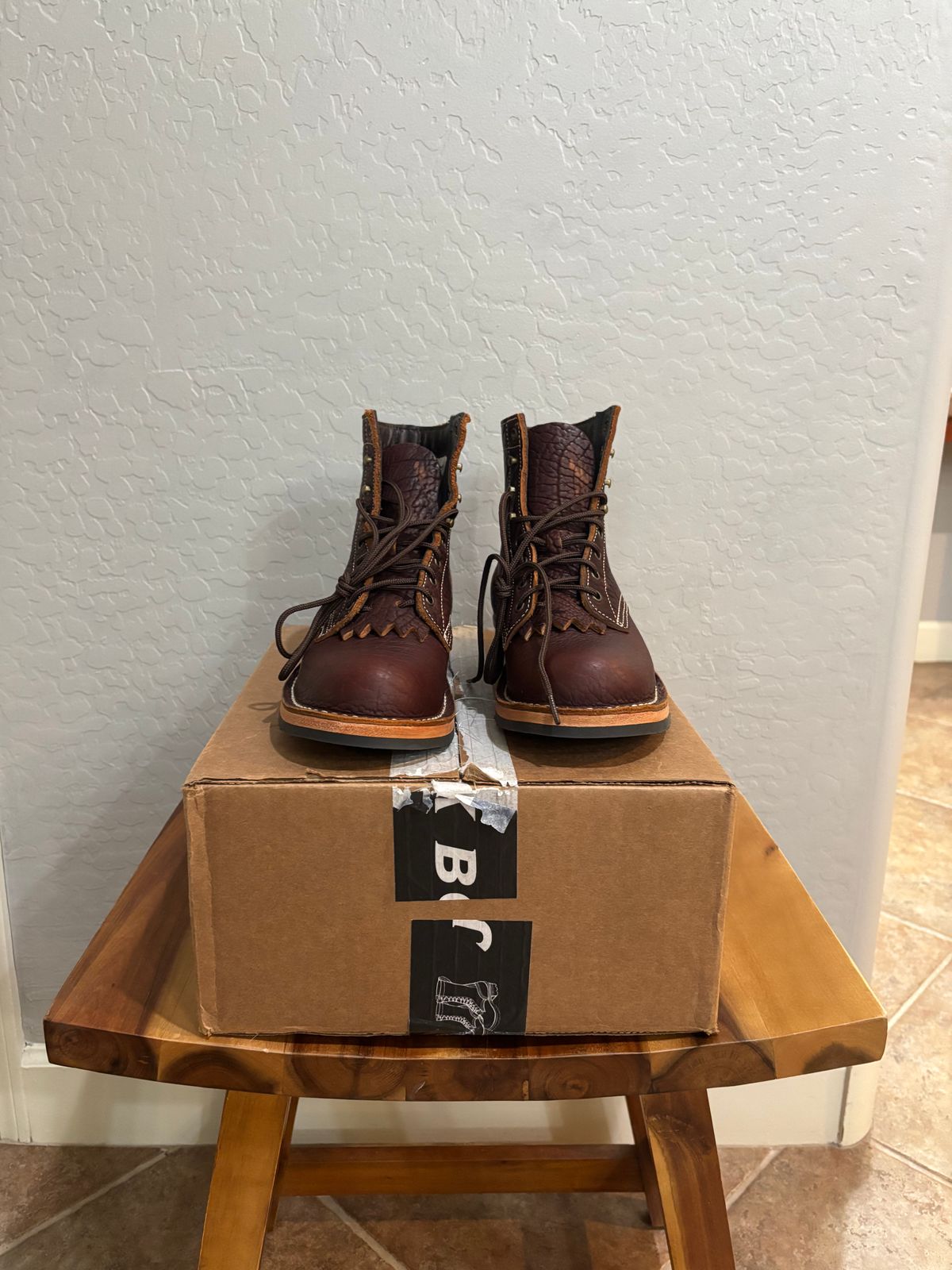 A pair of brown leather lace-up boots sitting on top of their cardboard box on a wooden stool