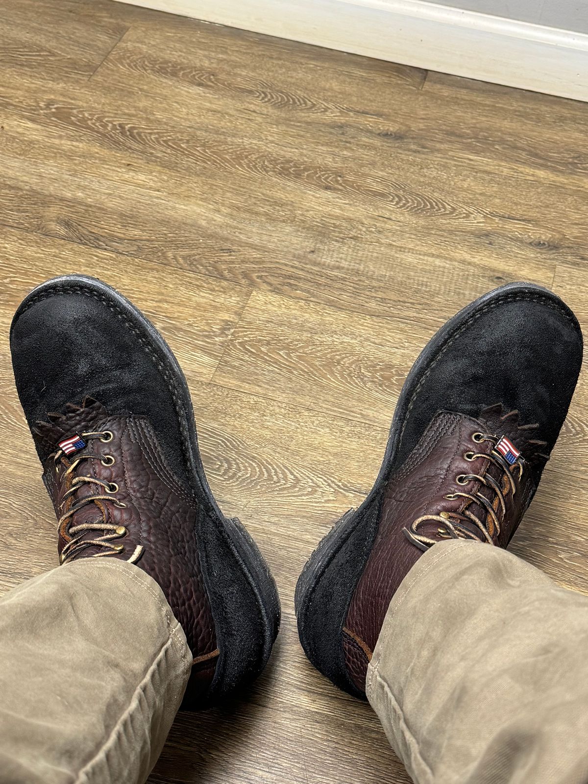 Person wearing brown and black lace-up boots standing on wood plank flooring