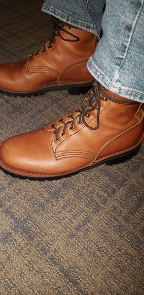 Brown leather lace-up boots worn with jeans on concrete ground