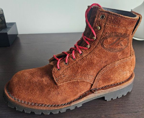Brown suede hiking boot with red laces on wooden surface