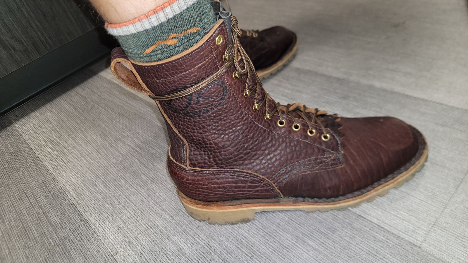 Brown leather work boots with laces worn with colorful striped socks on a wooden floor