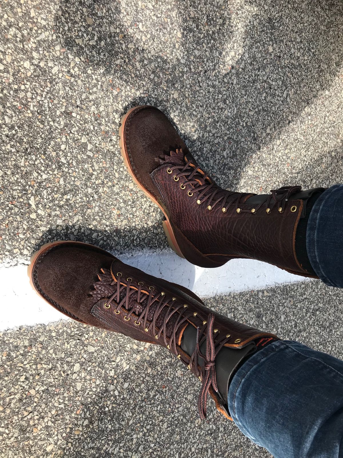 Person wearing brown leather boots with laces standing on cracked asphalt pavement