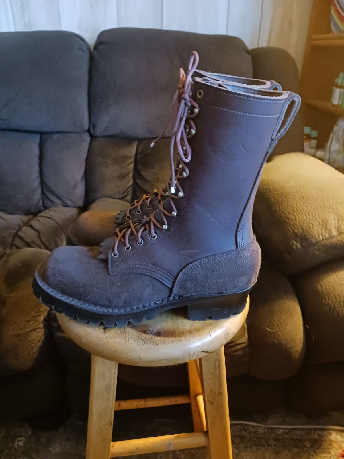 A pair of tall brown leather lace-up boots sitting on a wooden stool in front of a gray couch