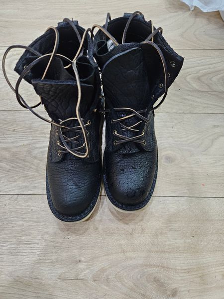 A pair of black leather boots with laces sitting on a wooden floor