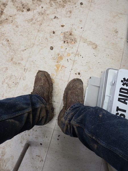 Person wearing muddy work boots and jeans standing on a stained tile floor next to a white medical kit or first aid box
