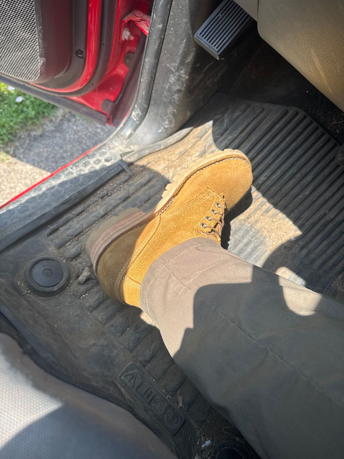 Person wearing tan work boots with feet positioned on car pedals inside vehicle