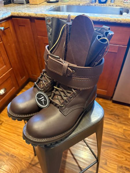 A brown leather work boot with laces and buckle straps sitting on a kitchen stool, with kitchen cabinets and countertop visible in the background