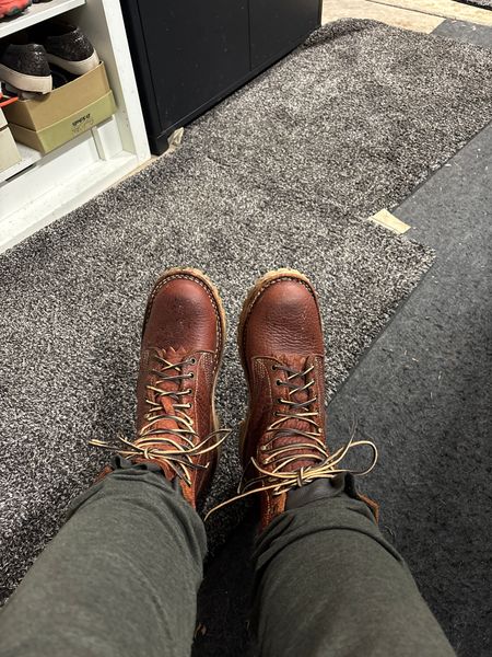 Person wearing brown leather lace-up boots standing on a doormat outside an entrance
