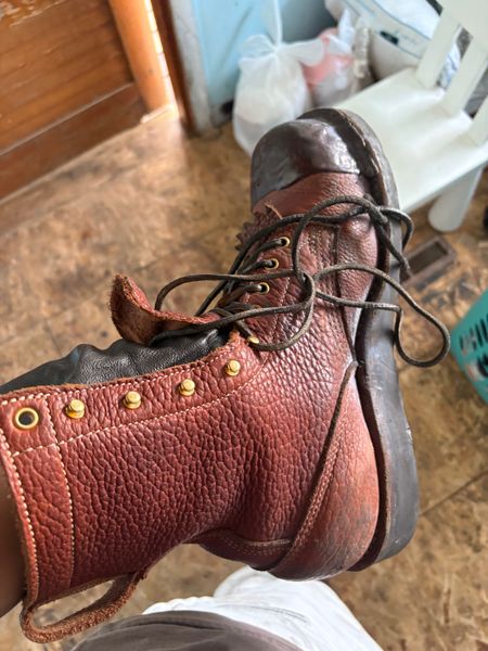 A brown leather boot or shoe with laces and decorative brass studs, photographed indoors on a wooden floor