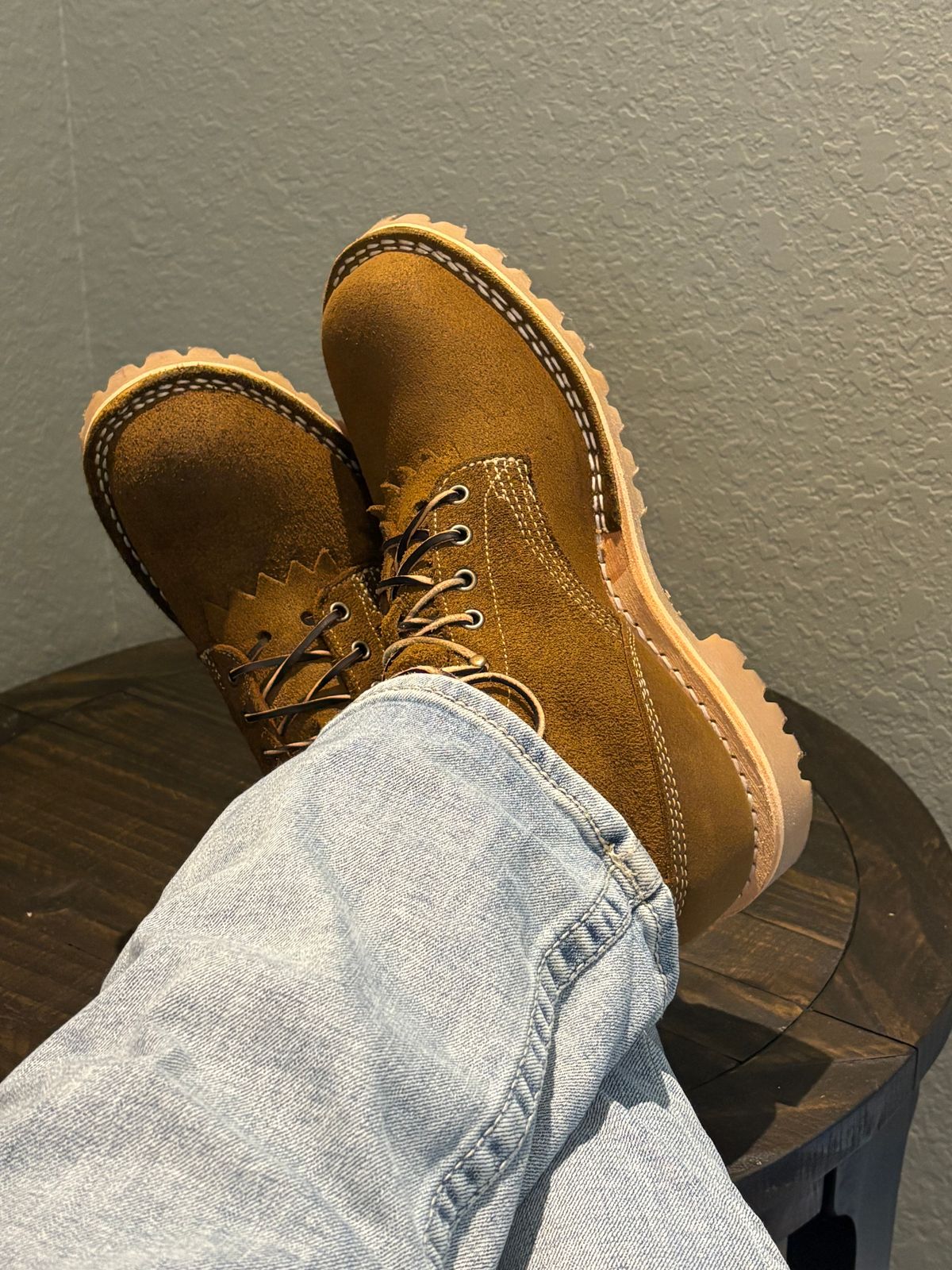 Person wearing brown suede boots with thick soles and light blue jeans, feet resting on wooden surface