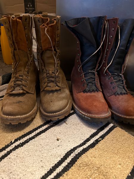 Two pairs of worn leather work boots sitting on a striped rug