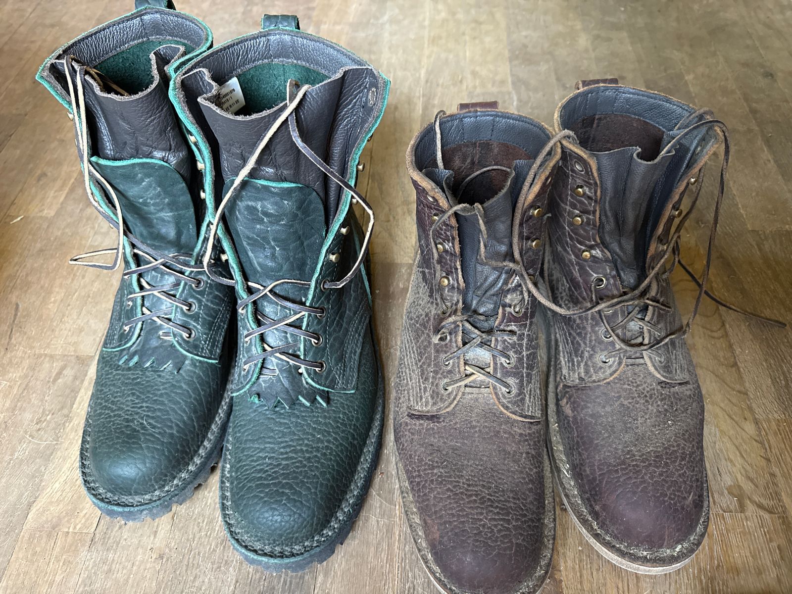 Two pairs of worn leather work boots on a wooden floor, one pair in dark teal and one pair in brown