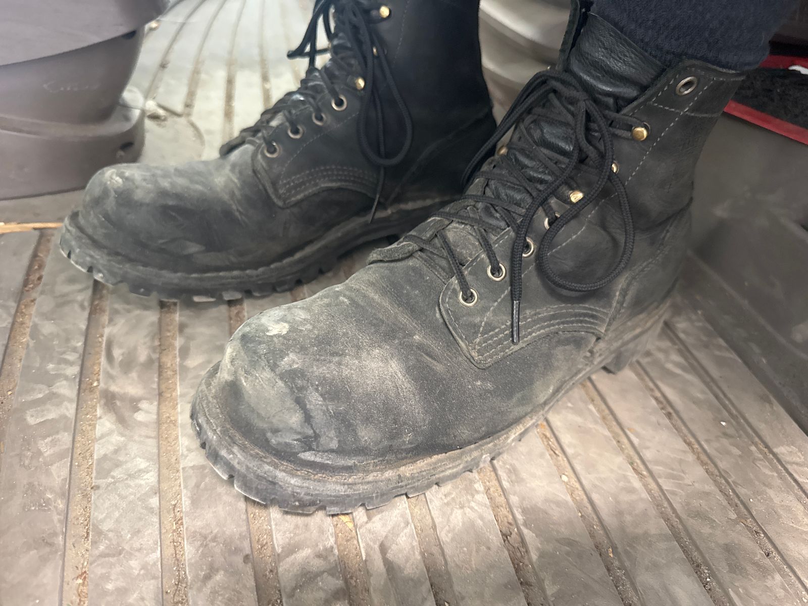 A pair of well-worn black work boots with laces sitting on wooden planks