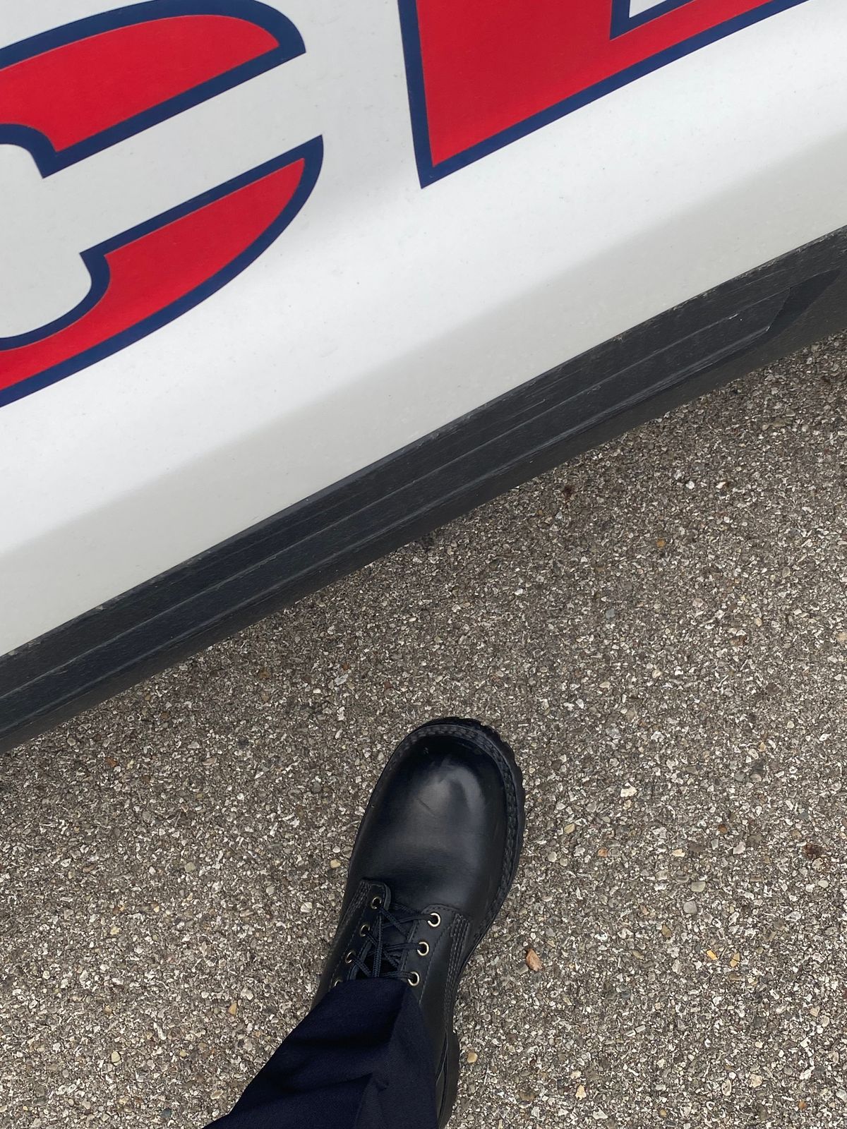 A black boot on asphalt ground next to a white vehicle with red and blue lettering