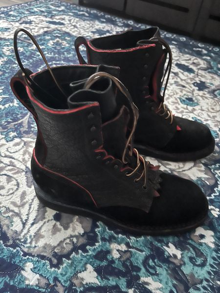 A pair of black boots with red trim and laces sitting on a patterned bedspread